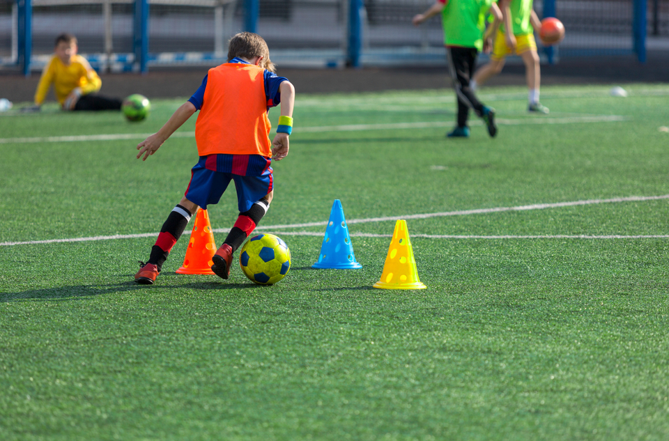 Grassroots football player at training dribbling ball round cones